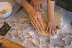 mani che tagliano biscotti ricavandoli dall'impasto con uso di formine